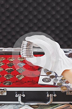 Hand in the white glove holds boxes with collector coins