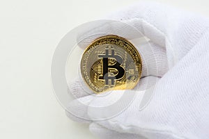 Hand with white gloves holding a golden bitcoin