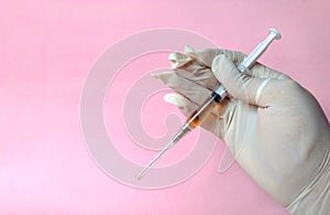 Hand with white latex glove with syringe ready to use on pink background. medical concept