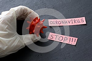 Hand in white latex rubber glove holds red coronavirus sample model on black background. Coronavirus outbreak, coronaviruses