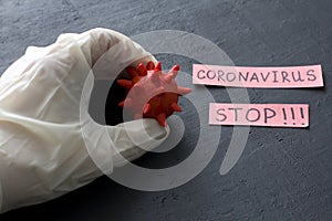 Hand in white latex rubber glove holds red coronavirus sample model on black background. Coronavirus outbreak, coronaviruses