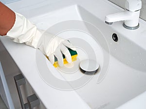 a hand in a white rubber glove with a sponge washes a white sink