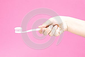 Hand with white toothbrush with toothpaste on pink background. H