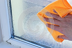 hand wipes off water condensation from plastic window glass in the room photo