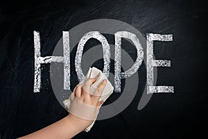 Hand wiping off chalk word HOPE on chalkboard using rag