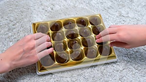 Hand of woman and boy is taking a chocolate candy from box, close-up view.