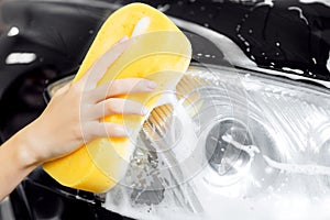Hand woman car wash foam with yellow sponge headlights