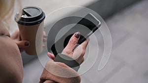 Hand of woman with coffee swiping across smartphone screen