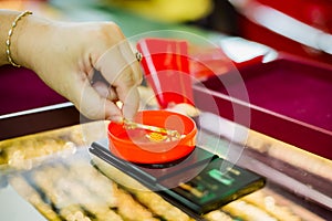The hand of woman customer is weighing gold jewelry with small digital scales