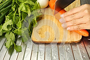 Hand of woman cutting carrots and vegetables on a wooden board.