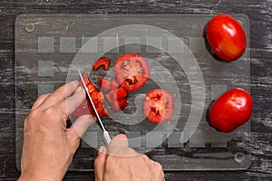 Hand of woman cutting fresh tomatoes with knife on the glass cut board on black background