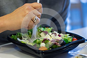 Hand of woman eating fast food salad with plastic fork