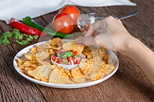 Hand of woman eating tortilla chips dip tomato salsa.