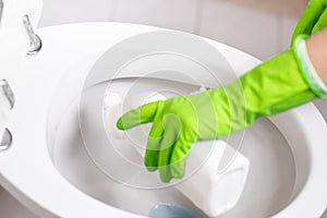 Hand of woman in green glove cleaning toilet