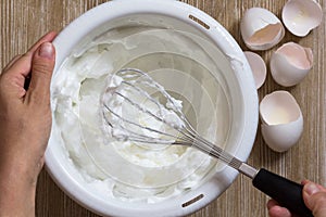 Hand of woman holding beater with whisked egg whites in the bowl photo