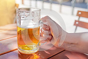 Hand of a woman holding a large mug of beer on beer garden table on sunny day