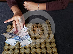 hand of a woman holding mexican banknotes and stacked coins of ten mexican pesos