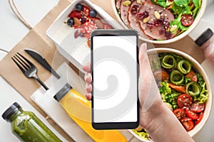 Hand of woman holds phone mock up screen over food boxes delivery service app.