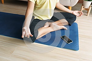 Hand of woman in lotus pose while sitting at mat yoga, Asian women practice yoga. With an online Trainer on mobile phone at home.