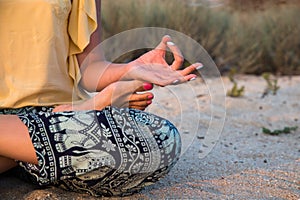 Hand of a woman meditating in a yoga pose on the beach at sunset