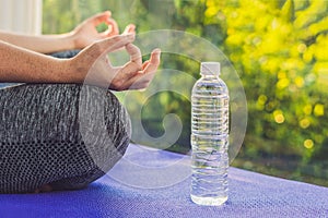 Hand of a woman meditating in a yoga pose on a rug for yoga and a bottle of water