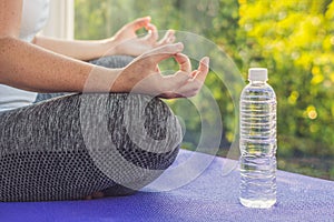 Hand of a woman meditating in a yoga pose on a rug for yoga and a bottle of water