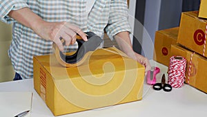 Hand of woman online entrepreneur using tape to packing parcel box at home office, prepare product for deliver to custome