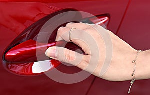 Hand of a woman opening the door handle of a red car