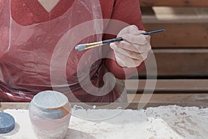 Hand of woman painting handmade clay vase with blue paint with brush