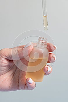 Hand of woman with pipette drop of serum with retinol on light background. Skin care treatment for aged skin..