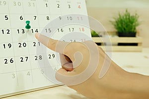 hand of woman point to day 14 on carlendar placed on wooden table and has plants in wood basket are background. image for