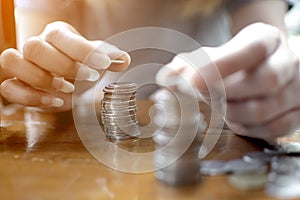 Hand of woman put a silver coin on top of two pile for stacking on the wooden table