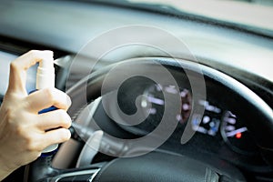 Hand of woman is spraying alcohol,disinfectant spray on steering wheel in her car,prevent infection of Covid-19 virus,