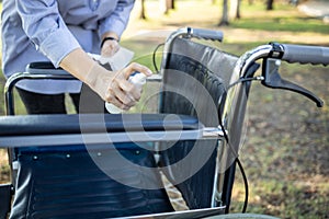 Hand of woman is spraying alcohol and wiping the dirt,disinfectant spray on wheelchair of senior,prevent the pandemic of Covid-19,