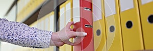 Hand of woman taking red ring binder from office archive