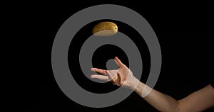 Hand of Woman Throwing a Potatoe against Black Background