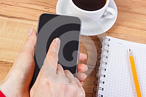 Hand of woman using mobile phone, notepad for writing notes, cup of coffee