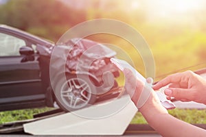 Hand of woman using smartphone and blur of her broken car parking on the road. Contacting car technician, Insurance or need help