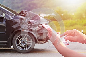 Hand of woman using smartphone and blur of her broken car parking on the road. Contacting car technician, Insurance or need help