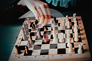 The hand of a woman in a vintage jabot rearranges wooden chess pieces on a chessboard. A logic game. Checkmate. The queen controls