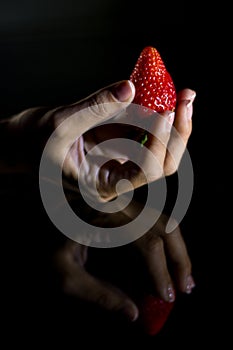 The hand of a woman who takes a strawberry and its reflection with black background