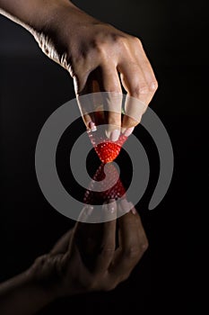 The hand of a woman who takes a strawberry and its reflection with black background