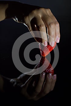 The hand of a woman who takes a strawberry and its reflection with black background