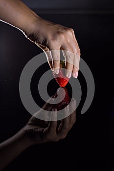 The hand of a woman who takes a strawberry and its reflection with black background