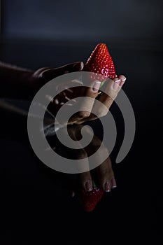 The hand of a woman who takes a strawberry and its reflection with black background