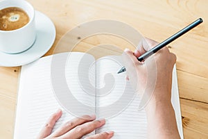 Hand of woman writing something in blank notebook