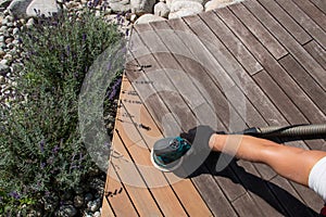 Hand of a wood repairman in protection gloves is sanding a deck with power sander tool