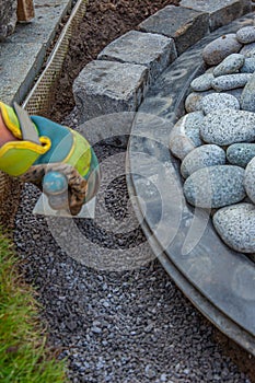 Hand with work glove arranging gritting material and basalt cobblestones into the curb of a garden fountain