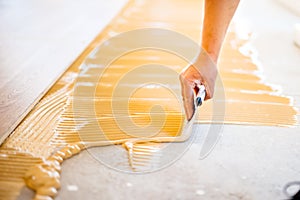 Hand of worker adding glue during parquet installation