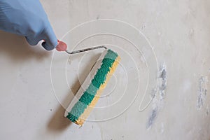 Hand worker in a blue glove holding a roller. The process of priming the concrete wall. The concept of apartment renovation,